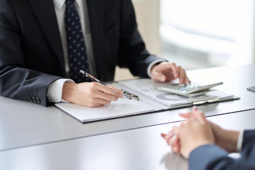 Zwei Personen in einem Büro überprüfen Diagramme auf einem Klemmbrett. Eine Person, wahrscheinlich ein Steuerberater, hält einen Stift.