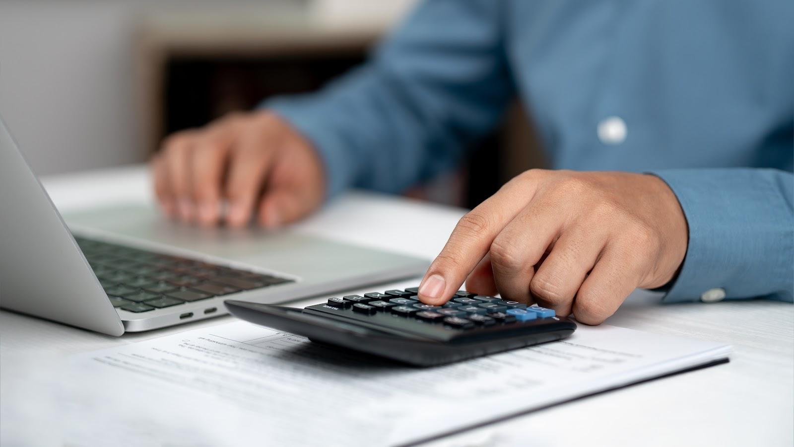 Eine Person prüft Finanzzahlen mit Taschenrechner und Laptop, um die korrekte Umsatzsteuervoranmeldung vorzubereiten oder Fehler zu korrigieren.